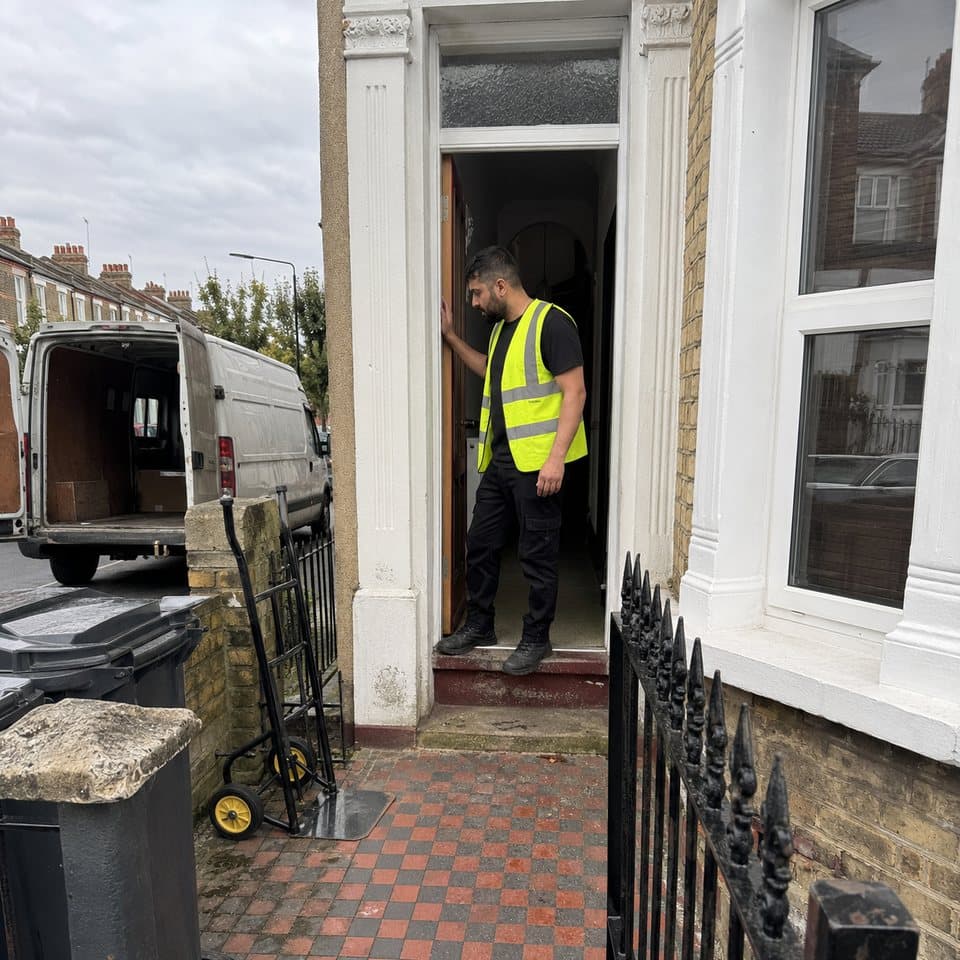 A removals worker in the open doorway of a London terraced house, checking the step with the van at the kerb behind him.